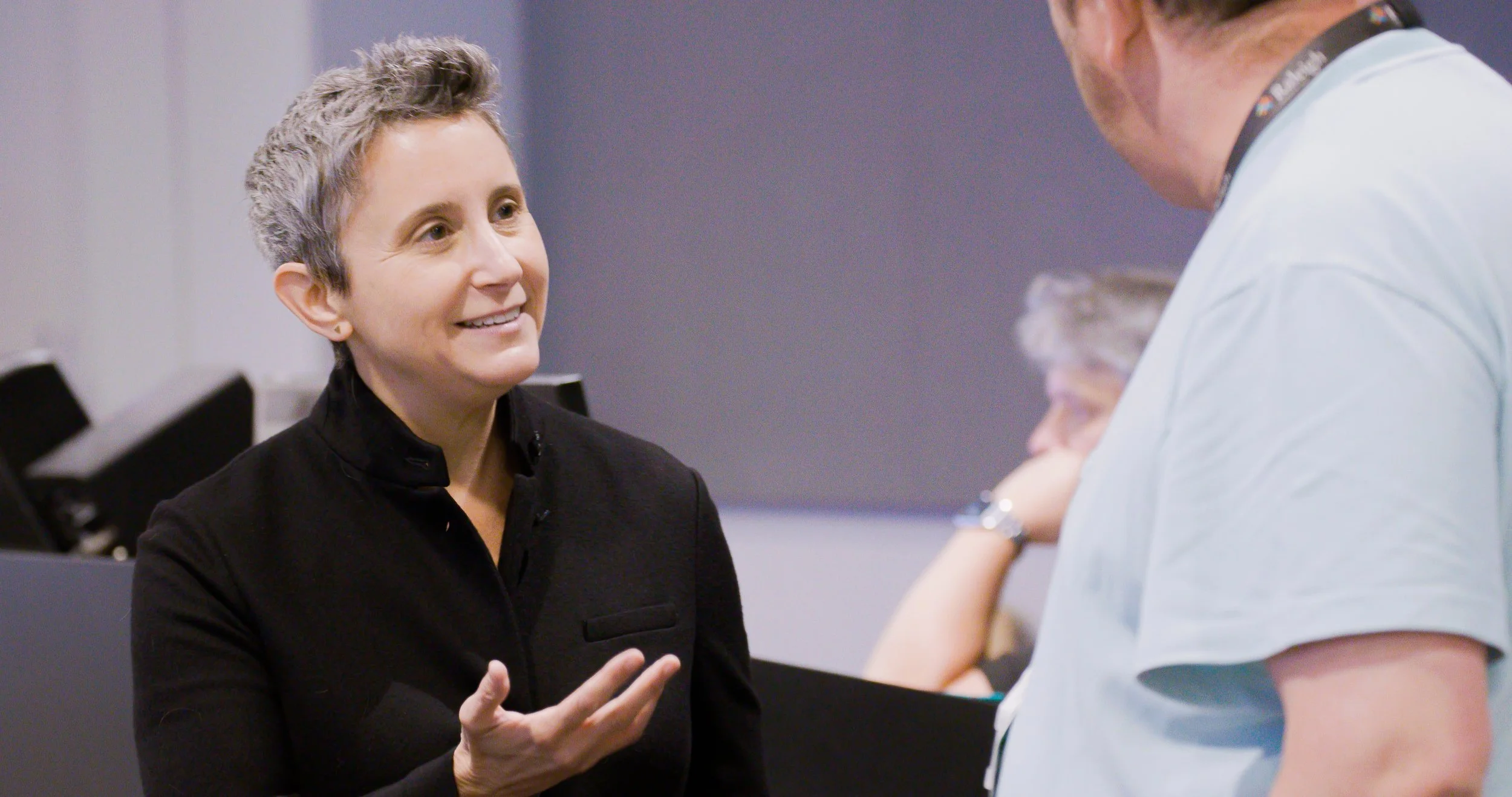 Keynote speaker Beth Sherman in a black blazer after an event smiling and speaking to a person in a light-colored shirt.