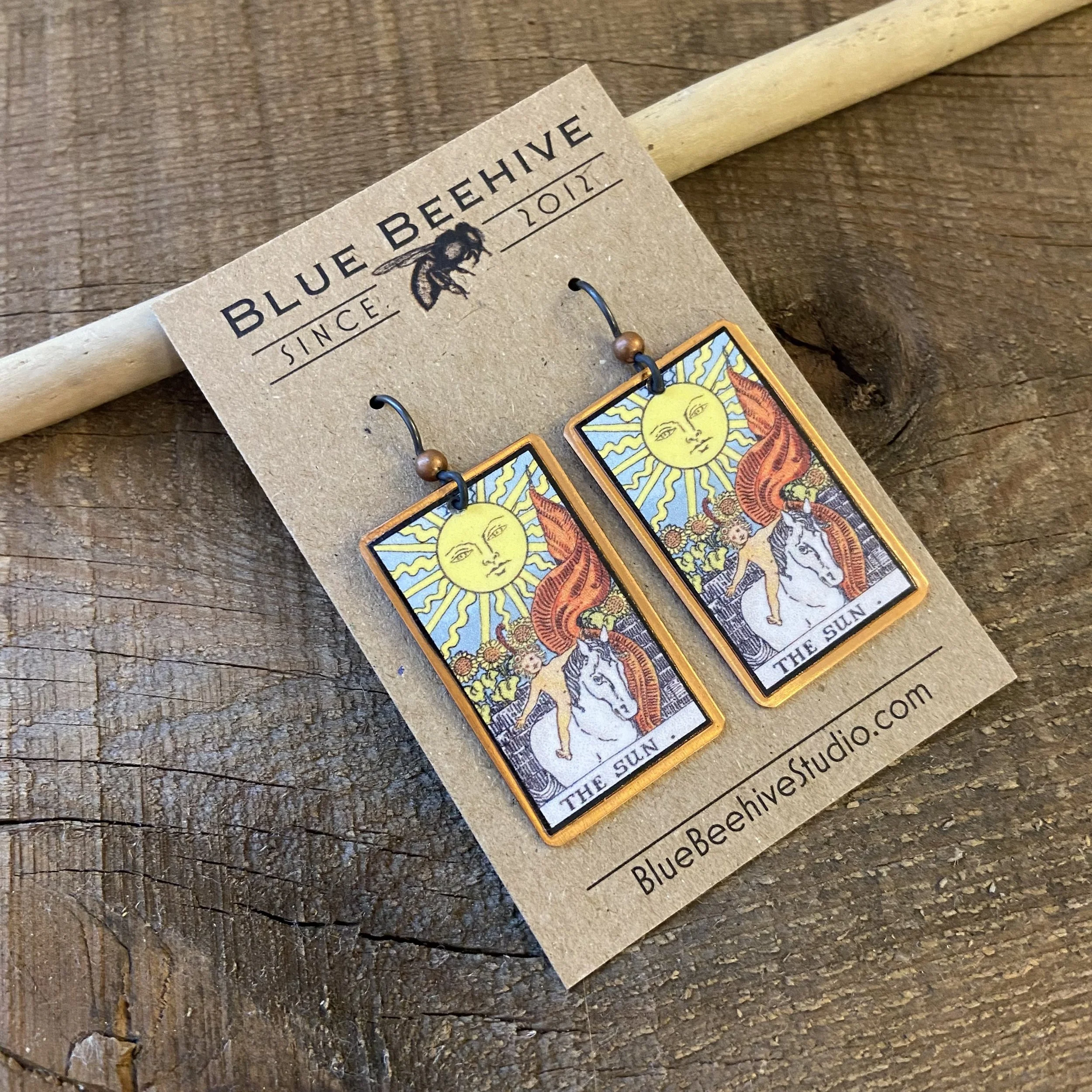 Picture of rectangular earrings of The Sun tarot card from the Rider-Waite Deck. Ear wires are black niobium with small copper balls.