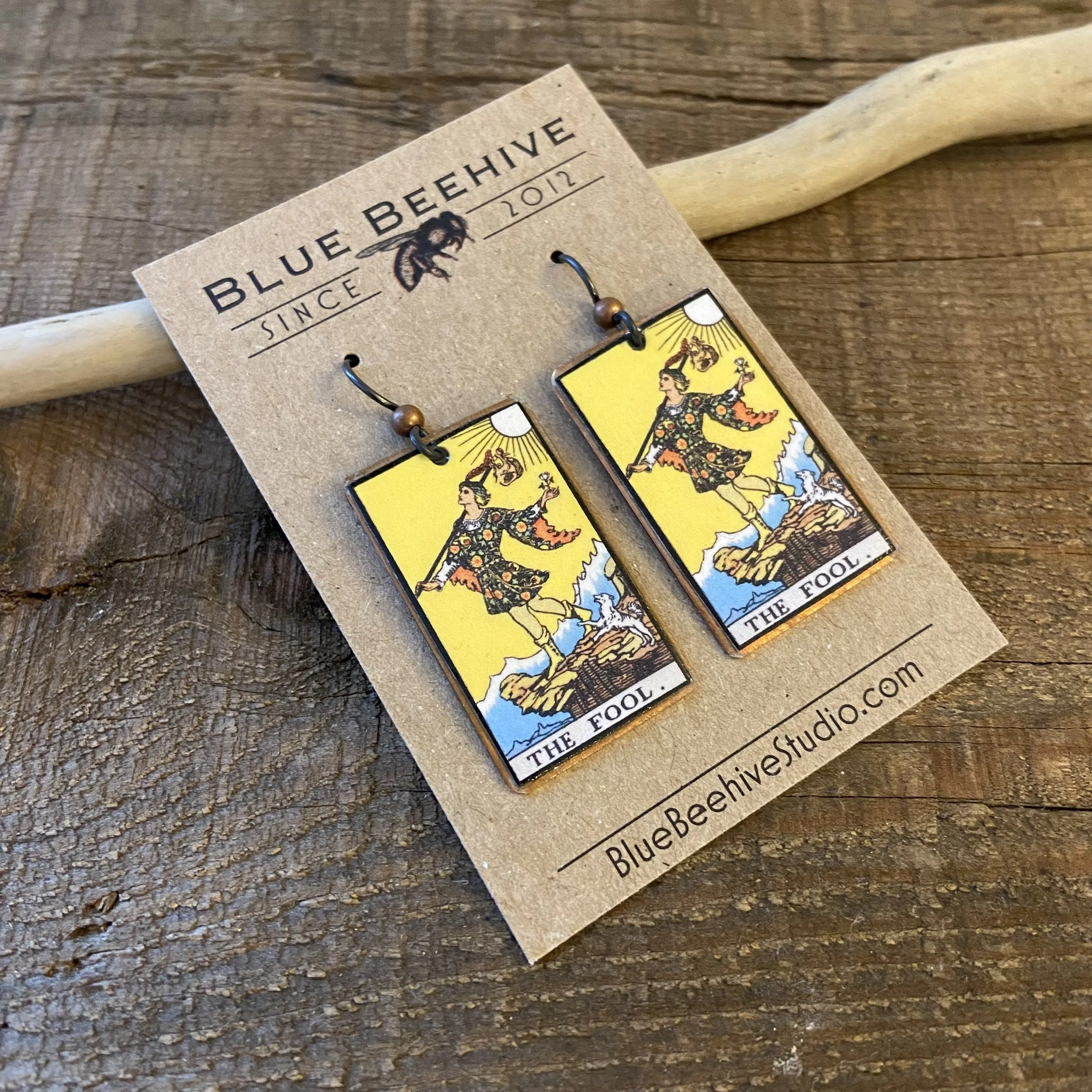 Picture of rectangular earrings of The Fool tarot card from the Rider-Waite Deck. Ear wires are black niobium with small copper balls.