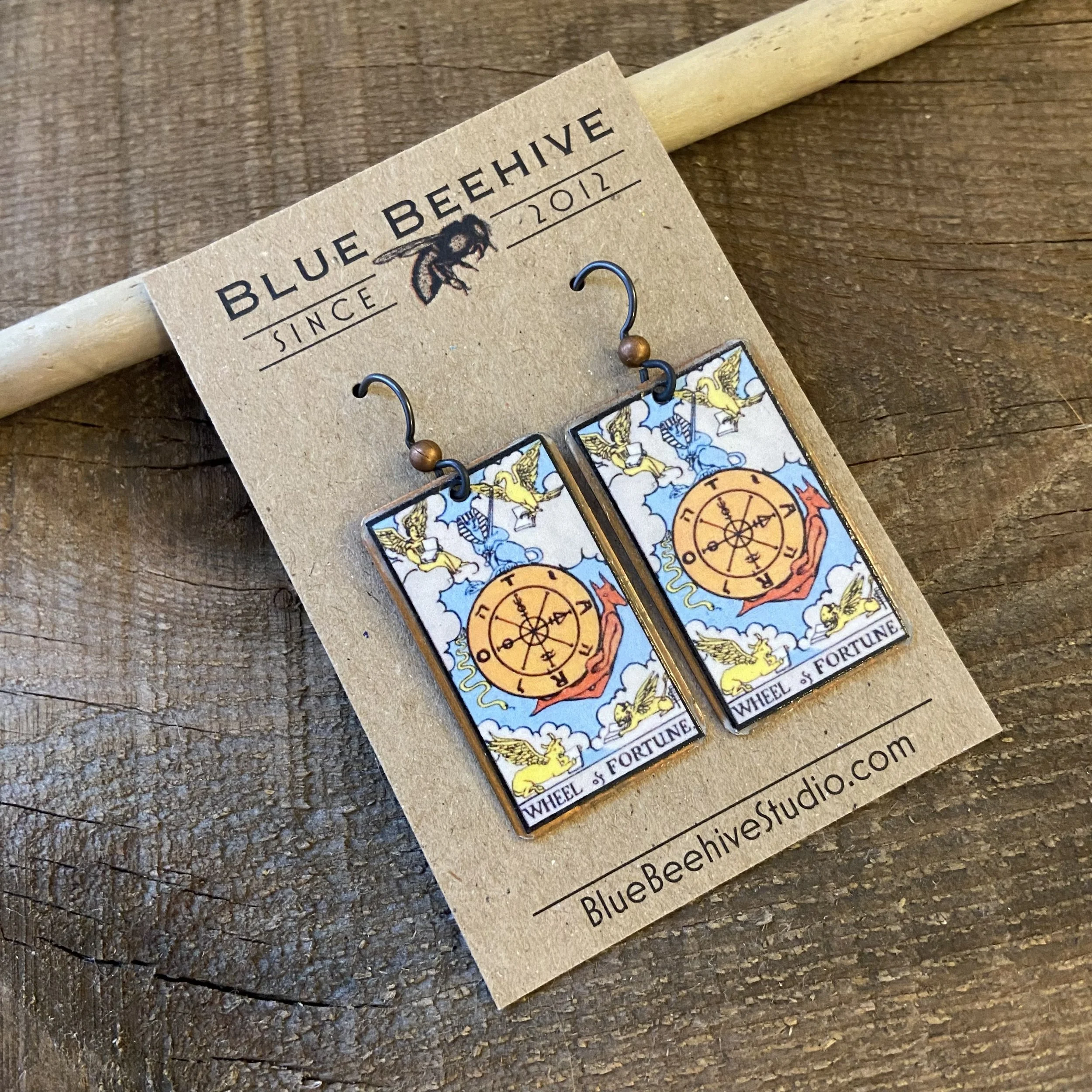Picture of rectangular earrings of the Wheel of Fortune tarot card from the Rider-Waite Deck. Ear wires are black niobium with small copper balls.