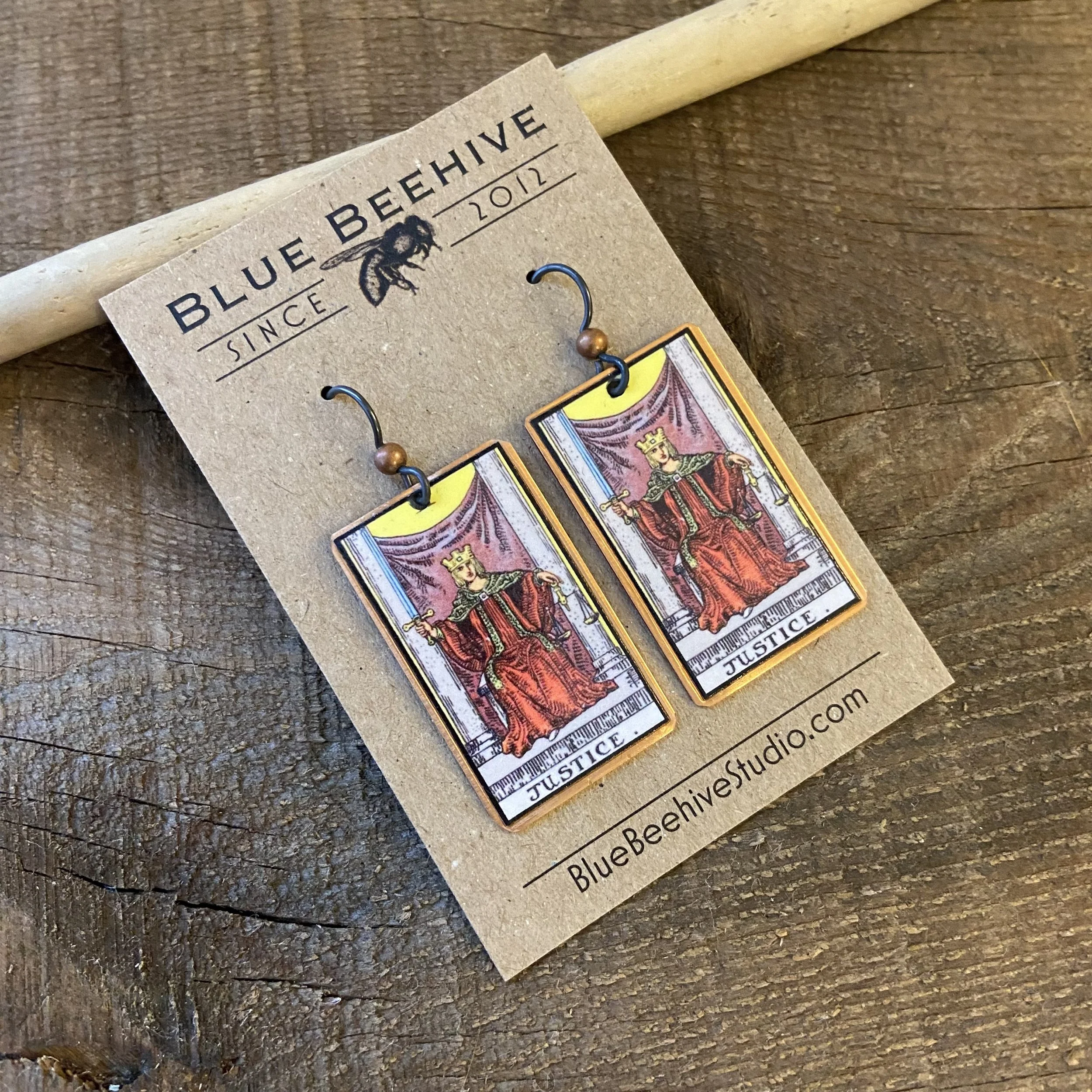 Picture of rectangular earrings of the Justice tarot card from the Rider-Waite Deck. Ear wires are black niobium with small copper balls.