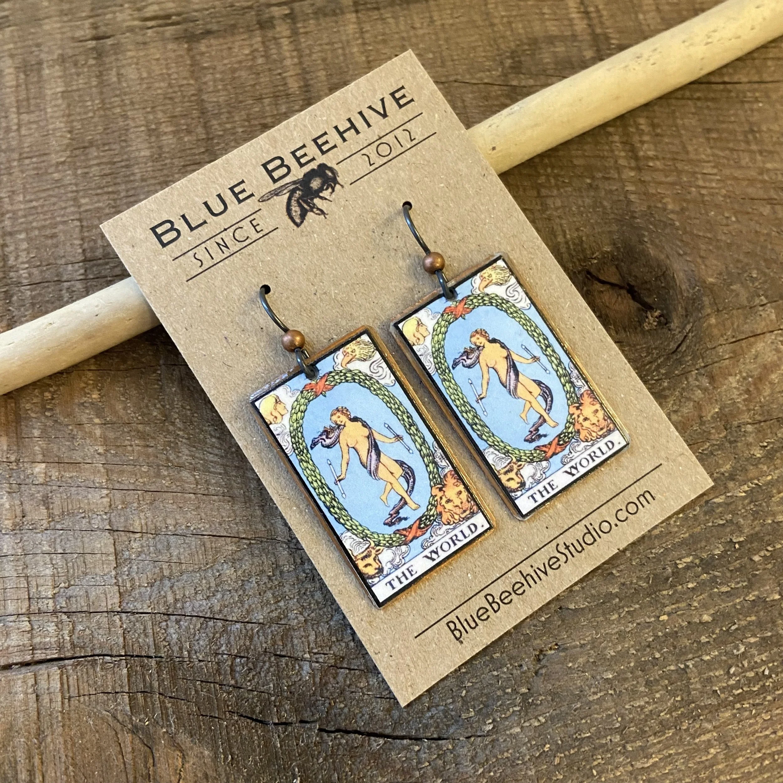 Picture of rectangular earrings of The World tarot card from the Rider-Waite Deck. Ear wires are black niobium with small copper balls.