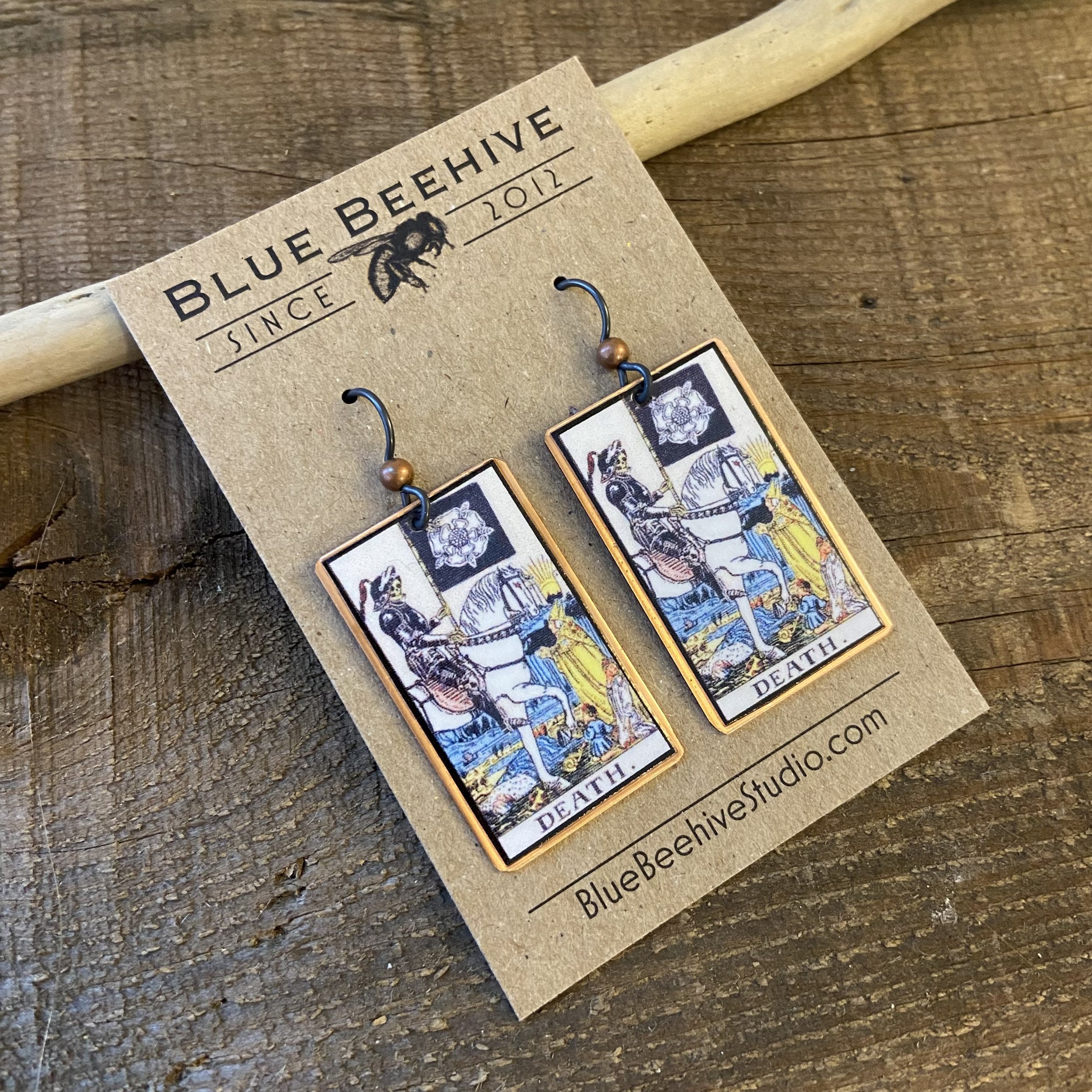 Picture of rectangular earrings of the Death tarot card from the Rider-Waite Deck. Ear wires are black niobium with small copper balls.
