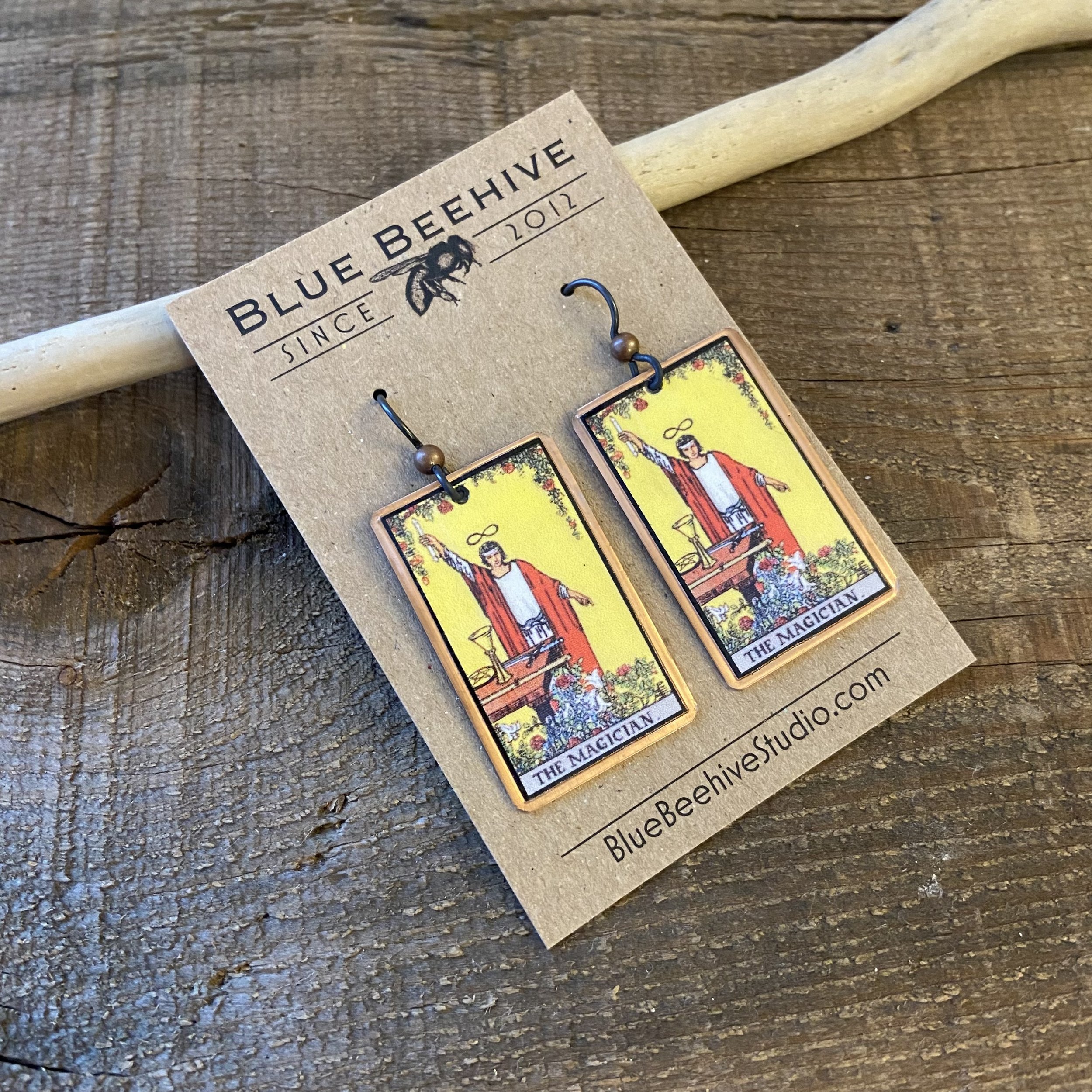 Picture of rectangular earrings of The Magician tarot card from the Rider-Waite Deck. Ear wires are black niobium with small copper balls.
