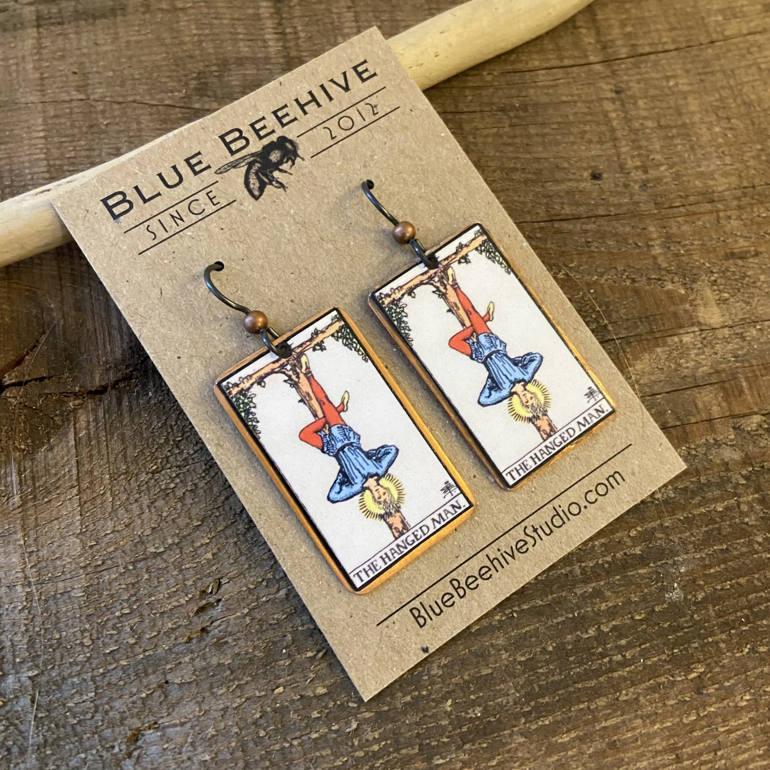 Picture of rectangular earrings of The Hanged Man tarot card from the Rider-Waite Deck. Ear wires are black niobium with small copper balls.