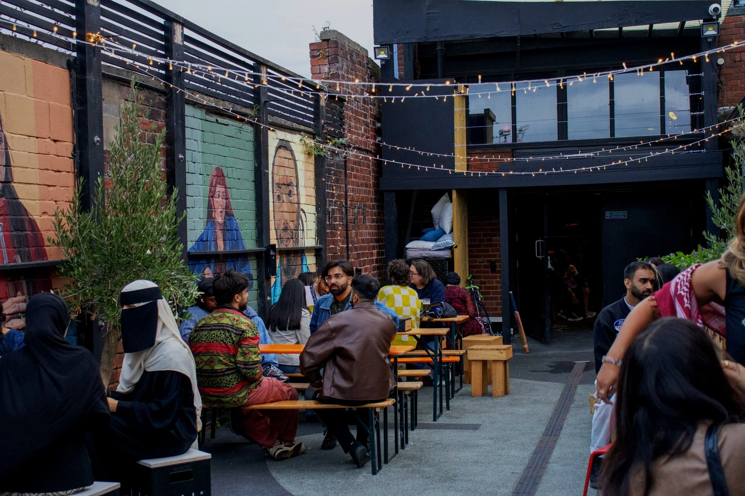 A crowded outdoor patio with people sitting on benches and tables.