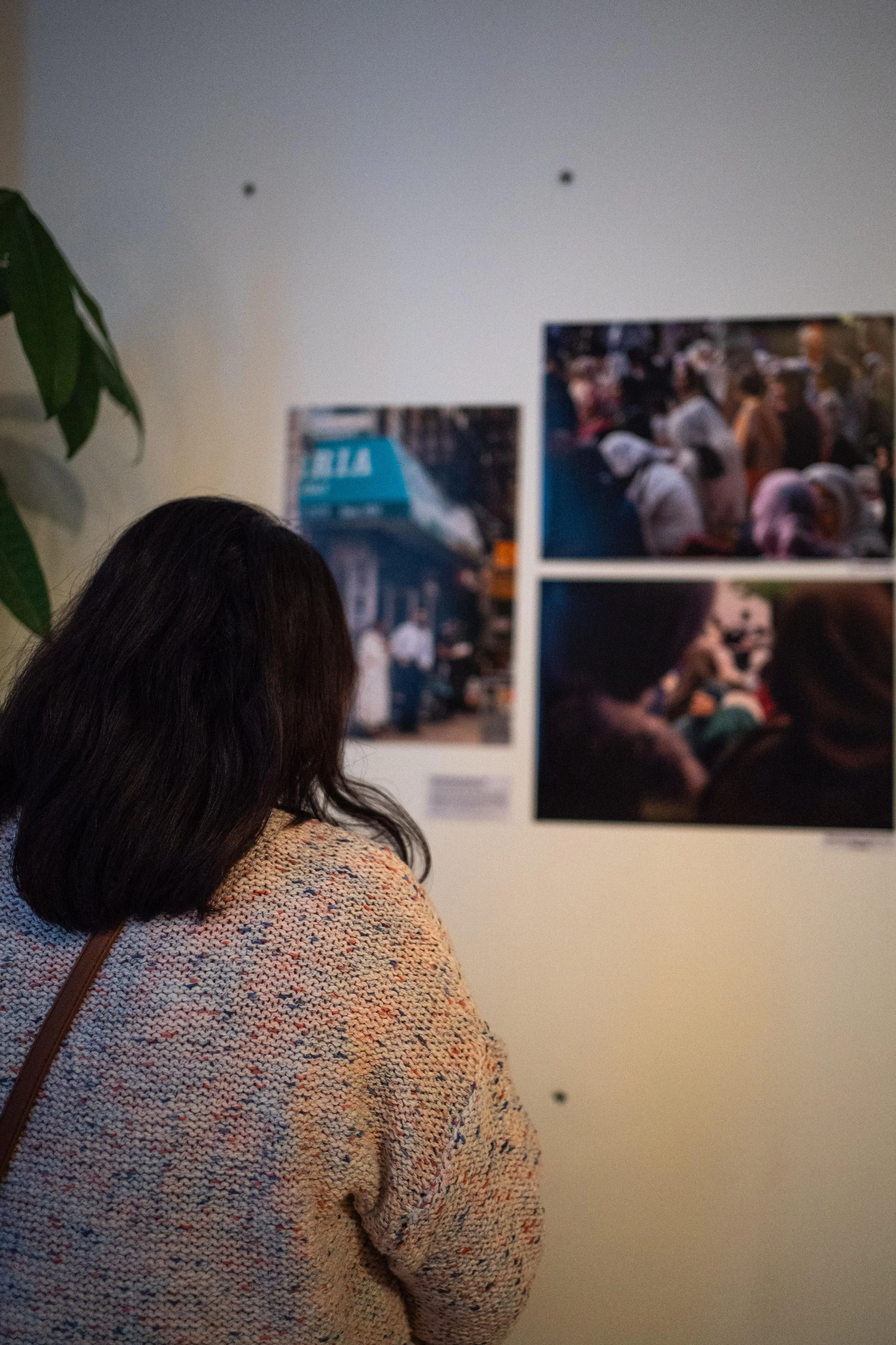A woman with dark hair wearing a multicolored sweater looking at artwork in a gallery.