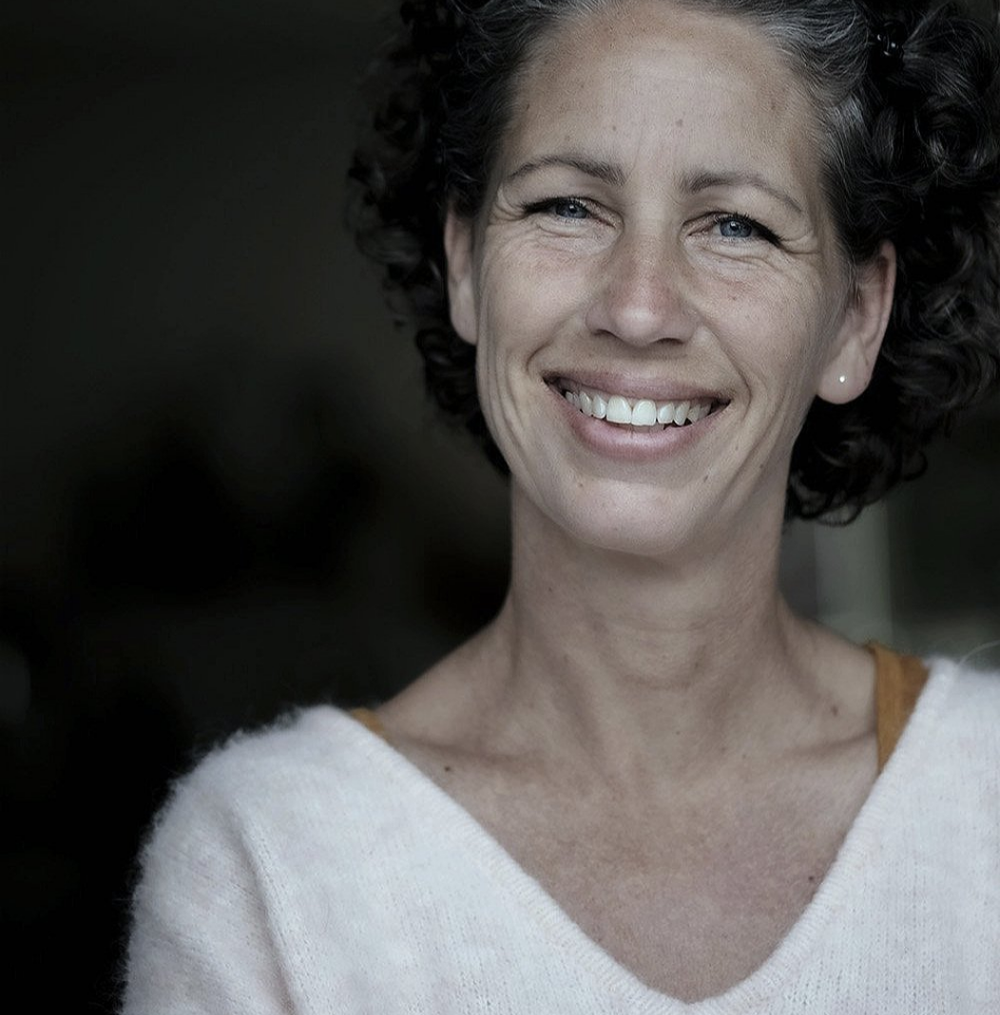 Portret van Xandra Dupper, lachend in een witte trui, in zwart-wit.