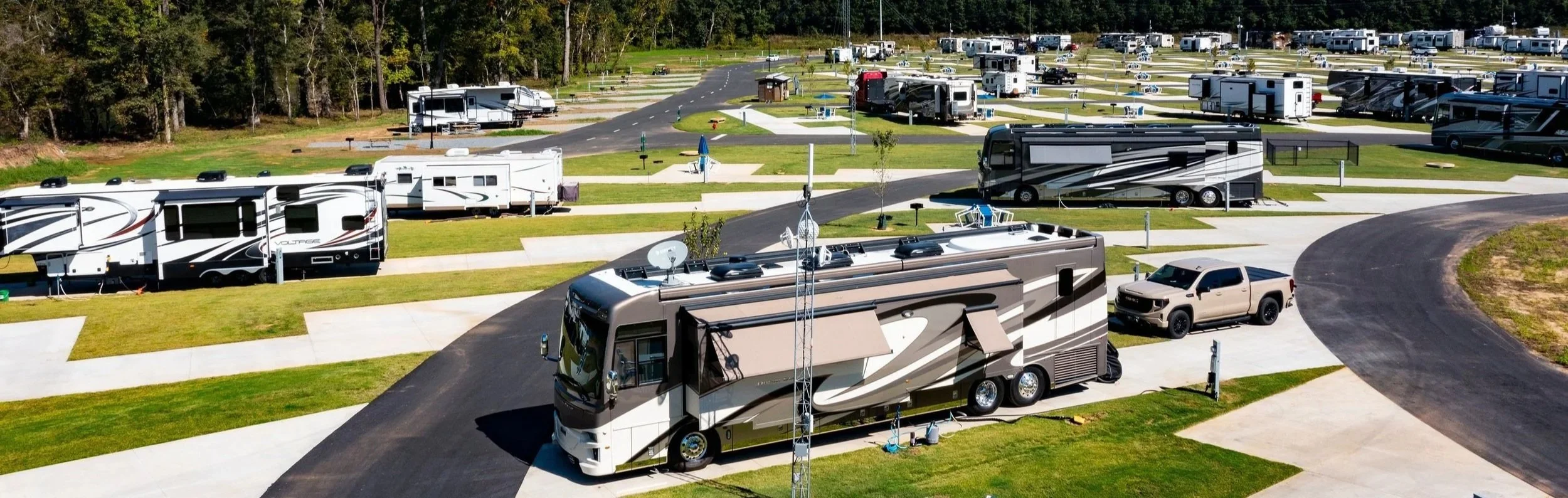 Aerial view of a campground with numerous RVs and trailers parked in designated spots, surrounded by grassy areas and trees in the background.