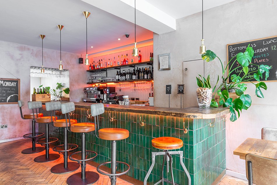 The bar and open kitchen inside Humble Grape Islington, bottles and glassware on the counter