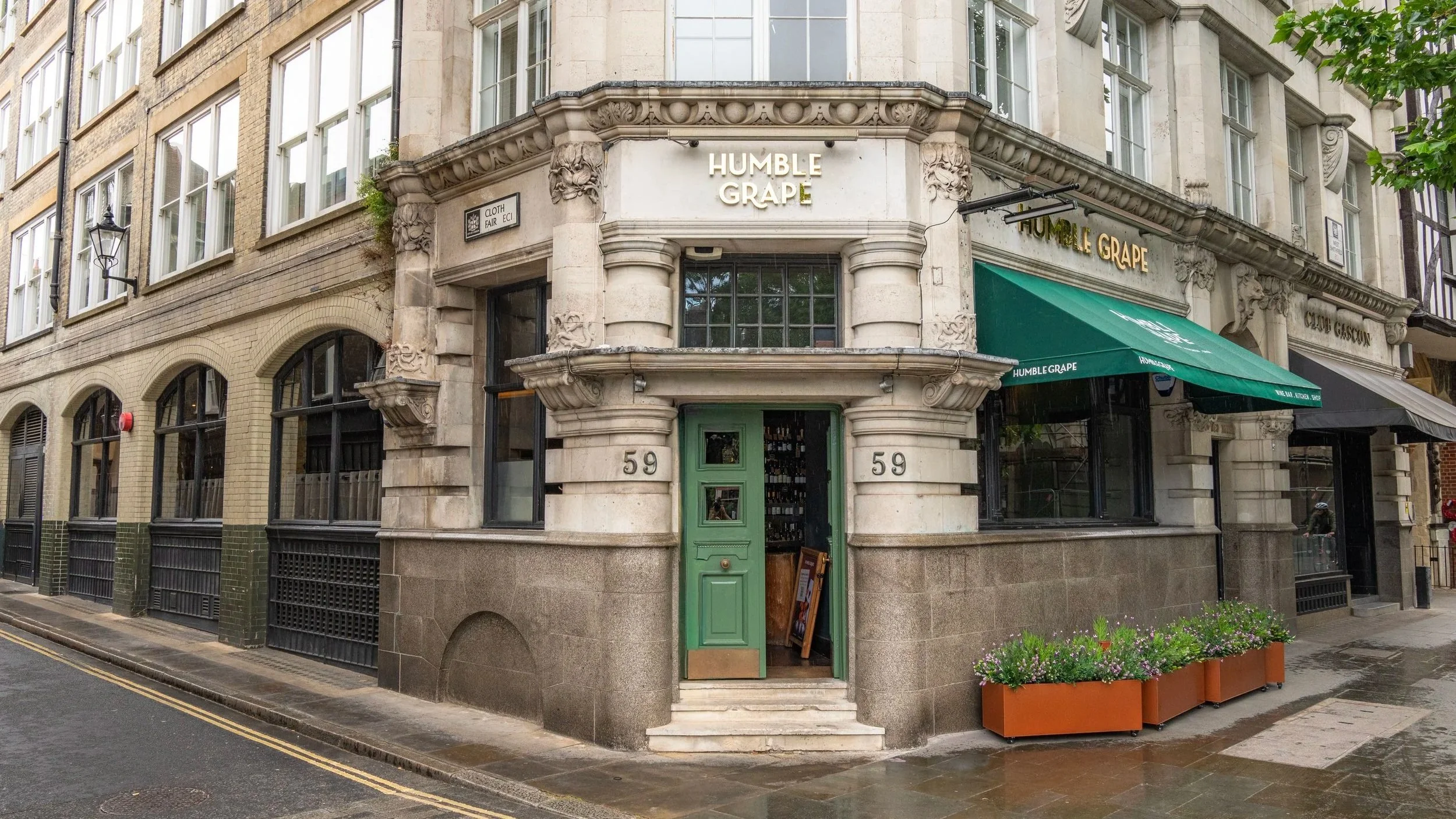 Corner storefront with green door, awning, and decorative architecture, with sign reading 'Humble Grape' on the building.