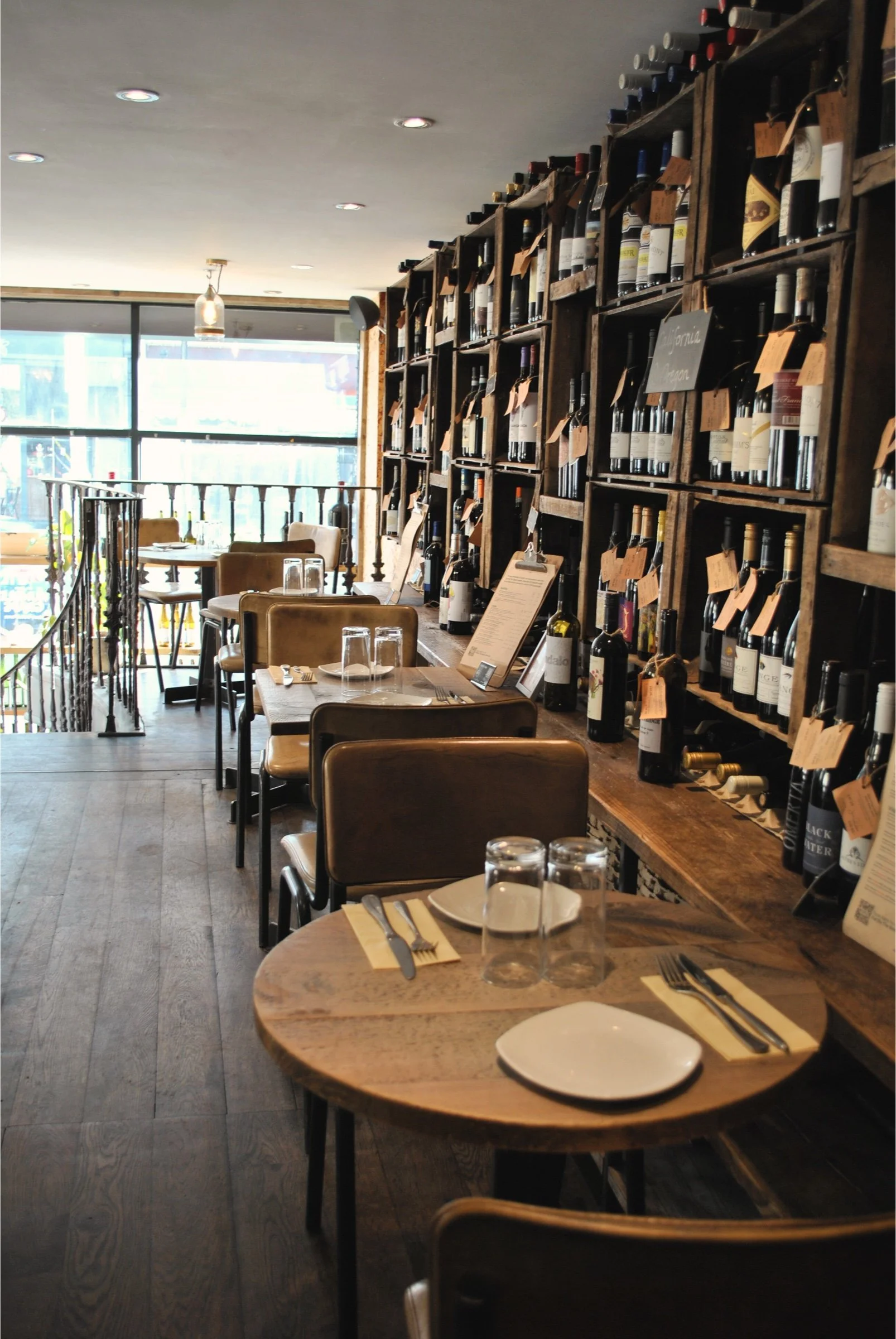 The dining room at Humble Grape Battersea, with set tables and a wall of wine bottles.