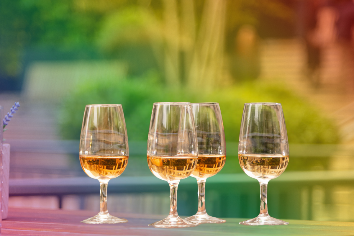 Four glasses of pink rosé wine on a patio table with a colorful blurred outdoor background