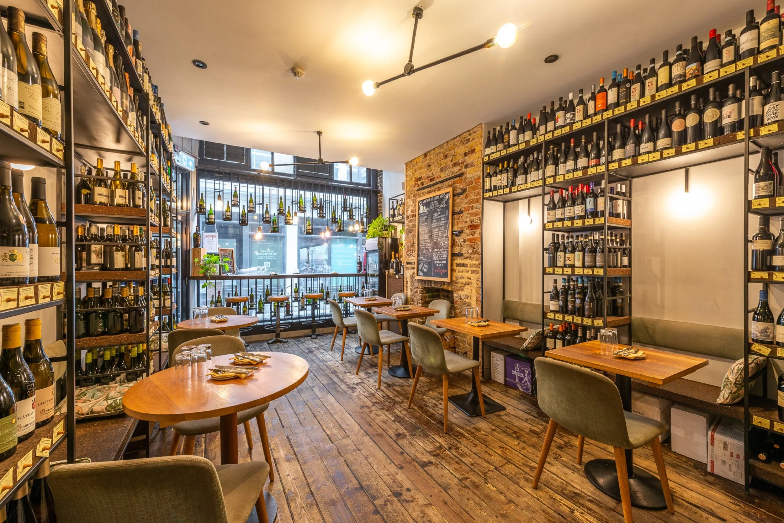 The Humble Grape Liverpool Street dining room, with wine-lined walls, warm wooden tables and a window onto the side alley.