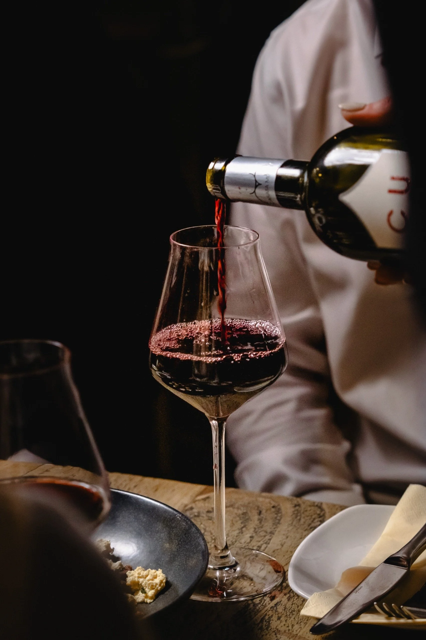 A Humble Grape team member pouring red wine beside a dining table.