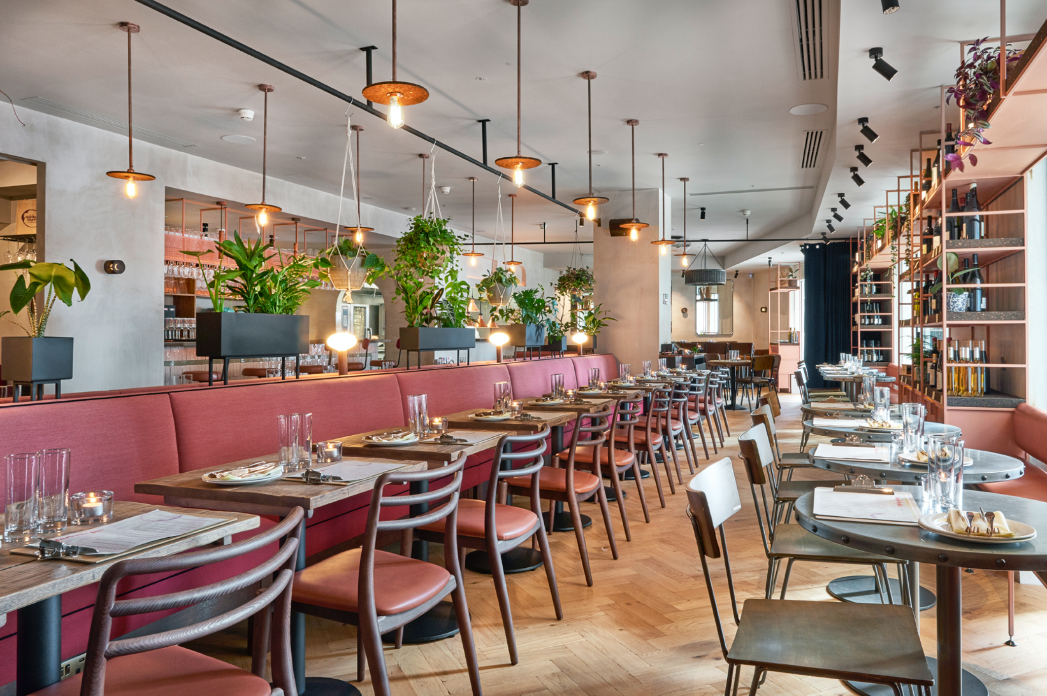 Humble Grape Canary Wharf's main floor, red banquette seating and wine shelving under pendant lighting
