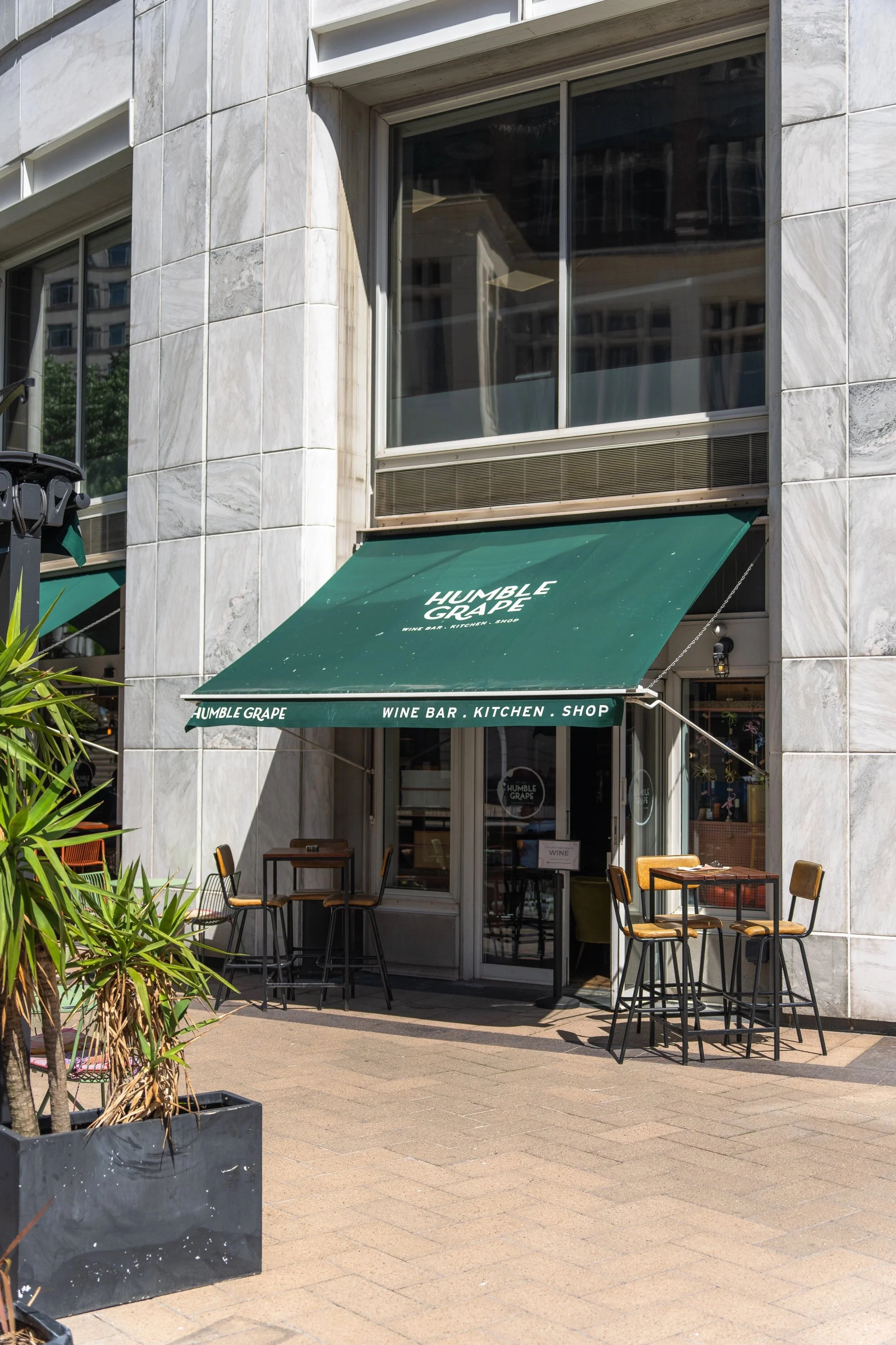 The Humble Grape Canary Wharf storefront and waterside terrace, with tables set beneath a green awning.