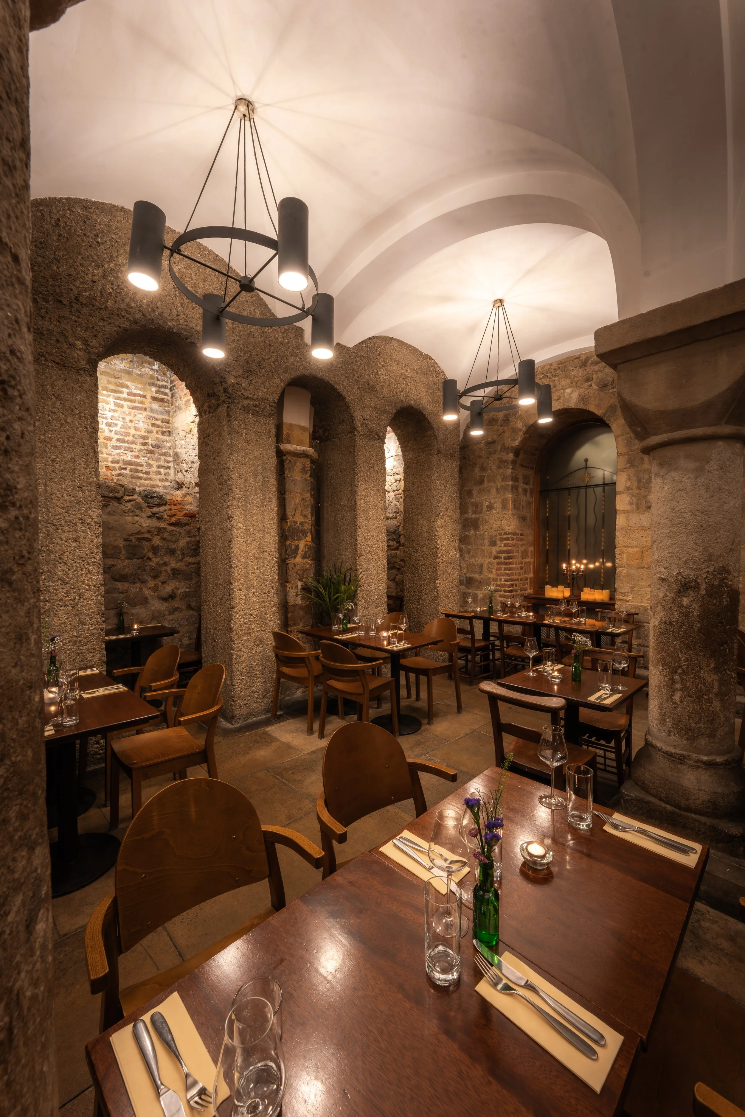 The vaulted stone crypt at Humble Grape Bow Lane, with black chandeliers hanging from the white arched ceiling.