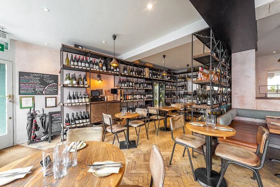 The Humble Grape Islington wine shop, with floor-to-ceiling bottle shelving beside the dining tables.