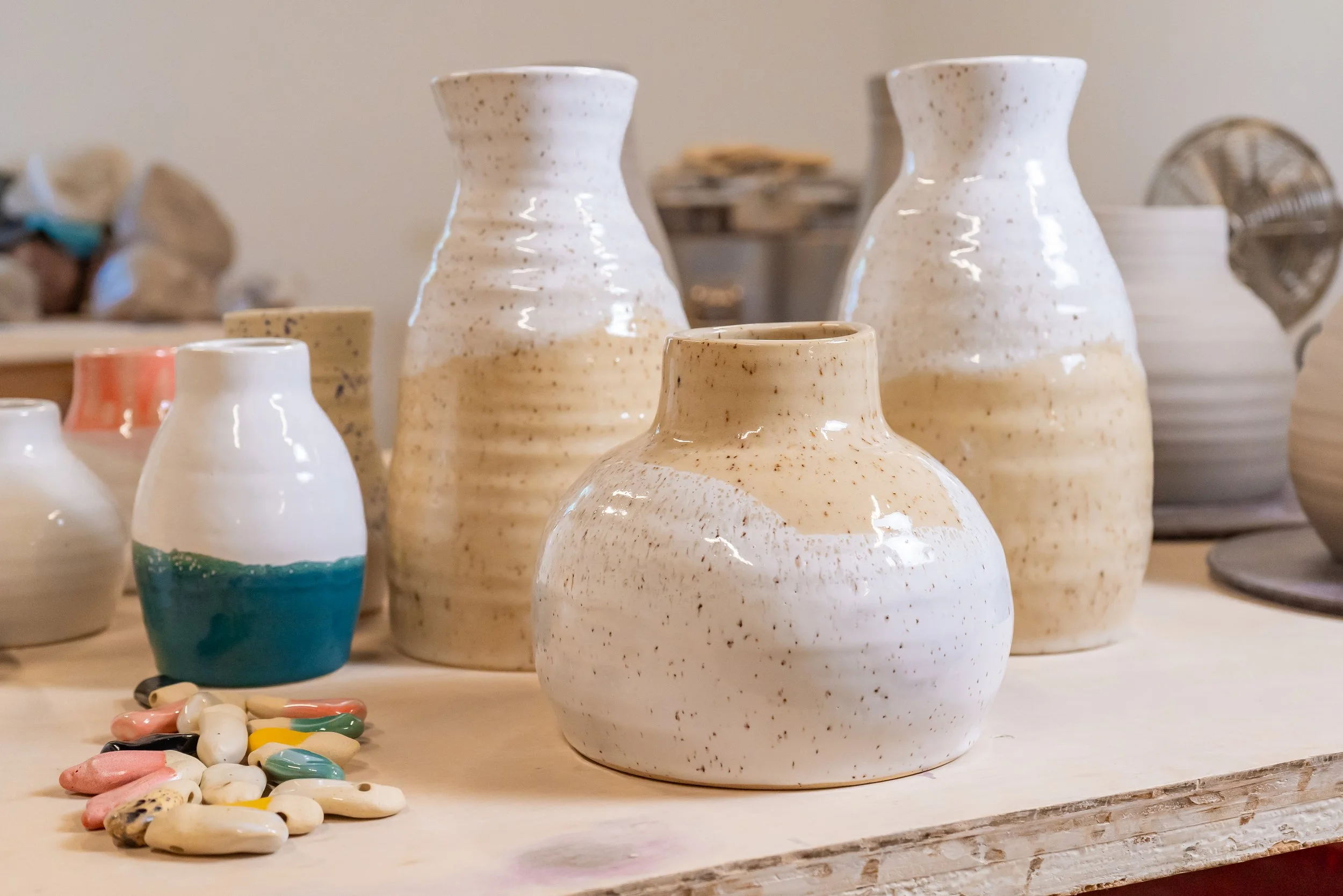 Various handcrafted ceramic vases and small colorful ceramic pieces displayed on a wooden surface.