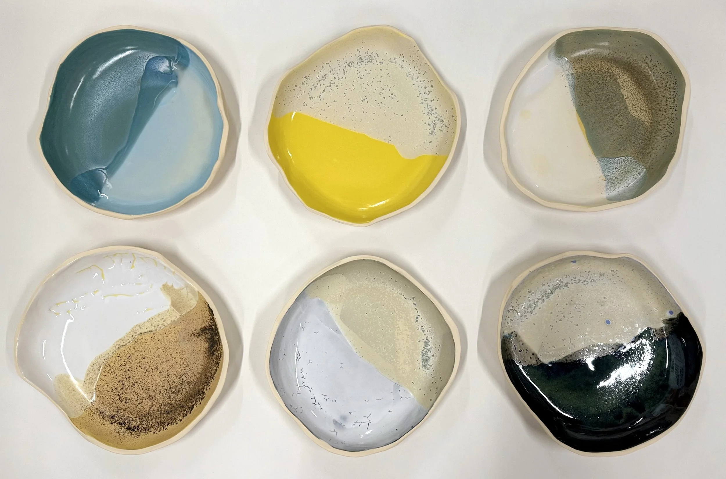 Six abstract ceramic bowls with different color patterns arranged in two rows on a white surface.