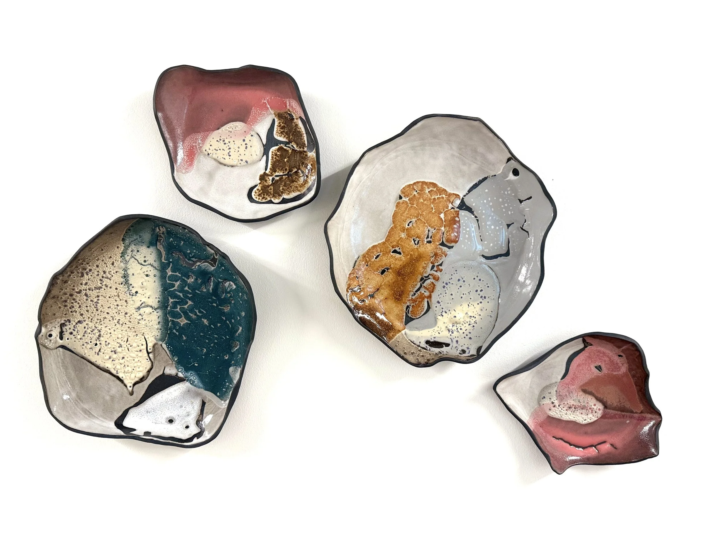 Four abstract glass bowls with mixed colors and textures, arranged on a white surface.