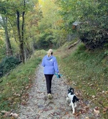 Carrie walking her dog on a wooded trail, embracing fresh air, movement, and the calm of body mind and spirit.
