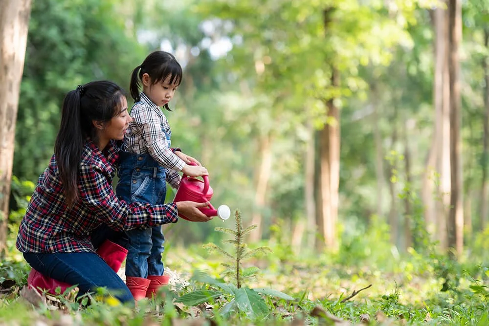 Mother and daughter watering a Little Saps tree seedling in the backyard