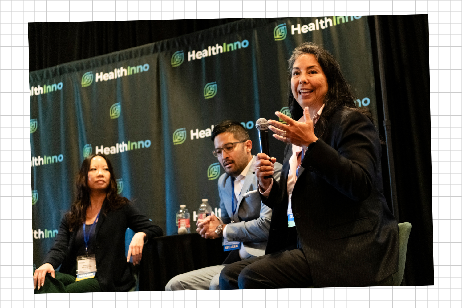 Three panelists speaking at a conference on a stage with a black backdrop displaying the 'HealthInno' logo. The woman on the right is holding a microphone.