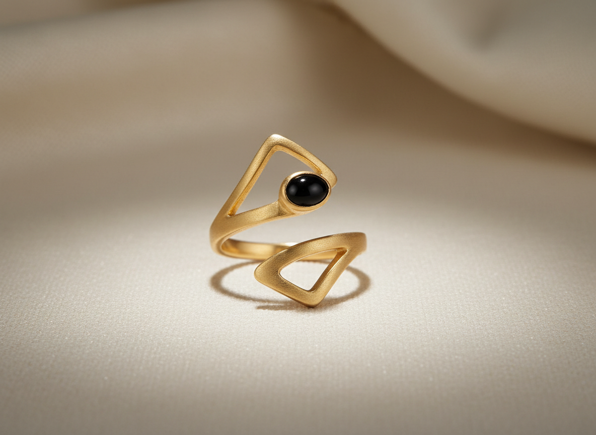 Gold open ring with black gemstone on a light, textured surface.