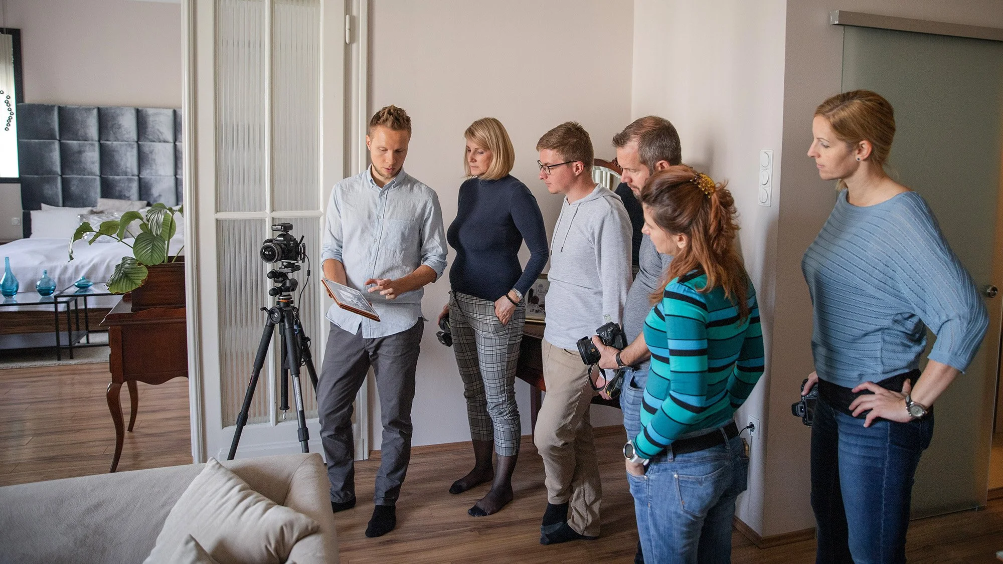 Team von sechs Personen bei einem Fotoshooting in einem Hotelzimmer, mit Kamera, Stativ und Equipment.