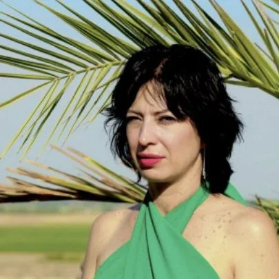 Frau mit schwarzem Haar, grüner Halstuch, steht vor Palmen im Freien