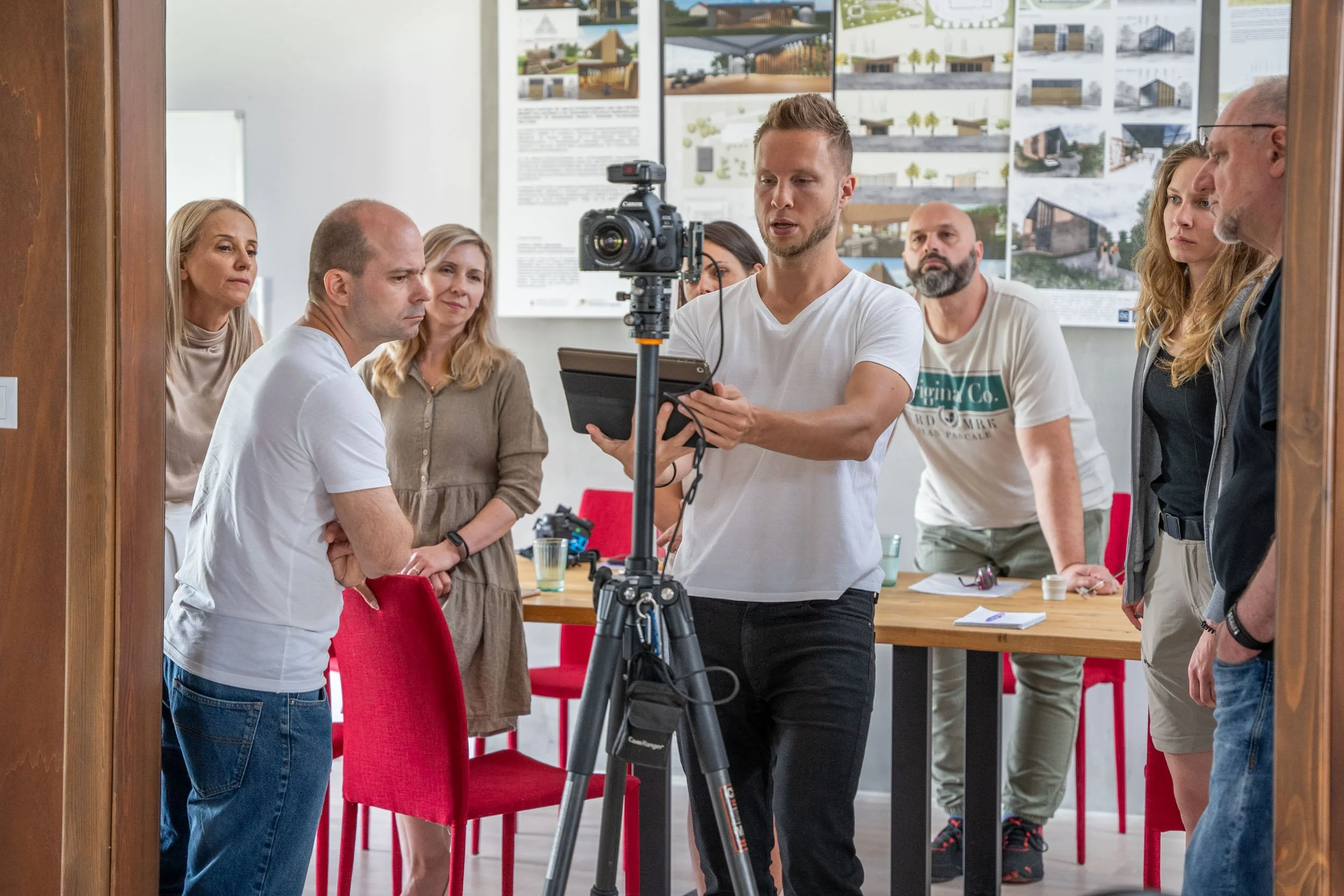 Menschen bei einer Präsentation im Raum, mehrere Menschen beobachten einen Mann, der eine Kameraeinstellung macht.