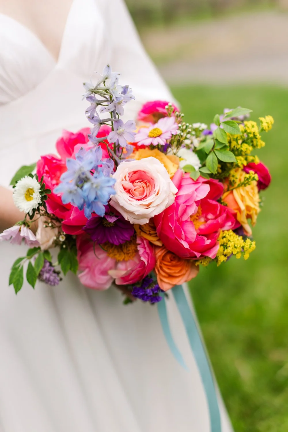 Person holding a colorful bouquet of mixed flowers, including roses, daisies, and wildflowers, outdoors.