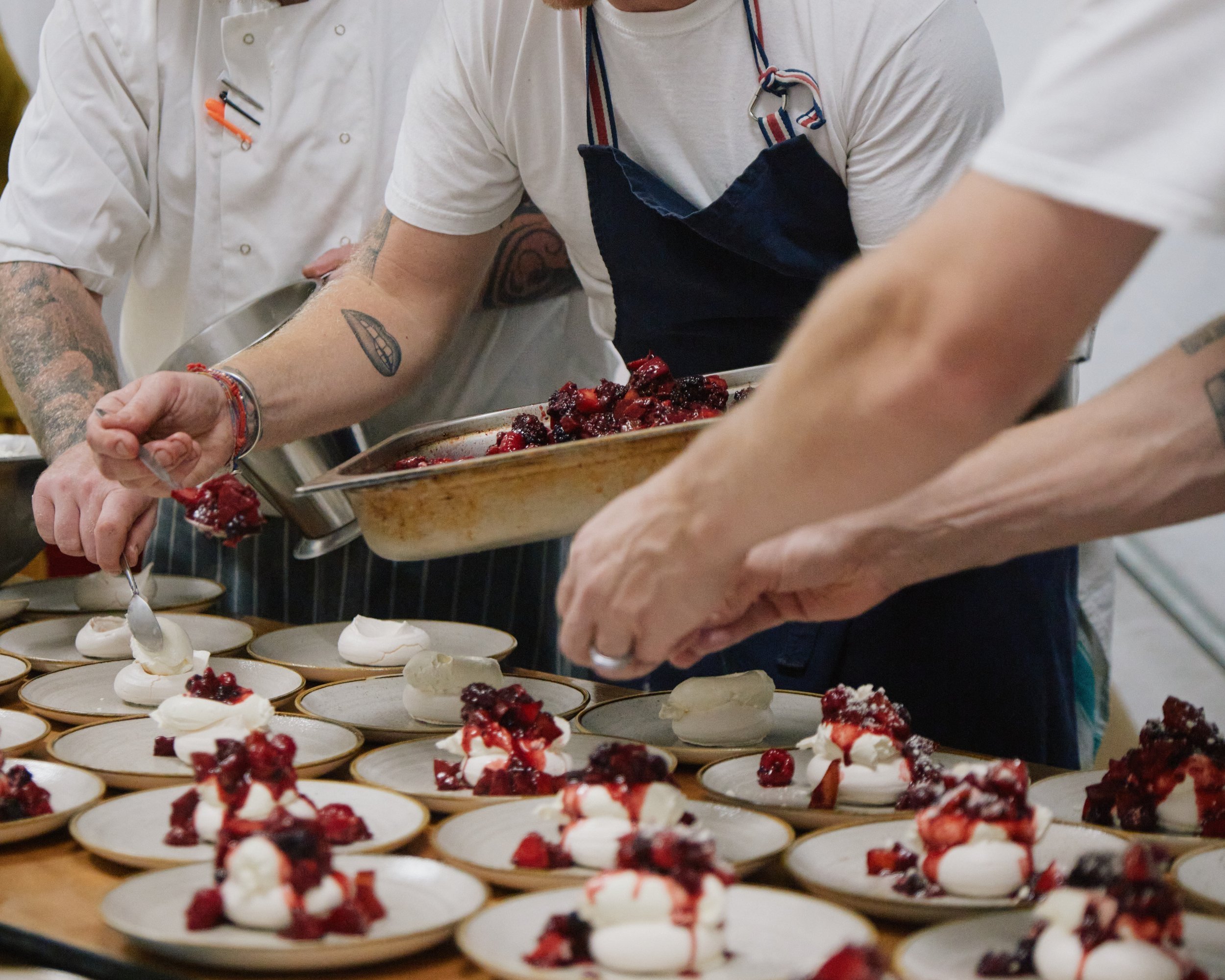 Chefs plating dessert with meringue and berry topping