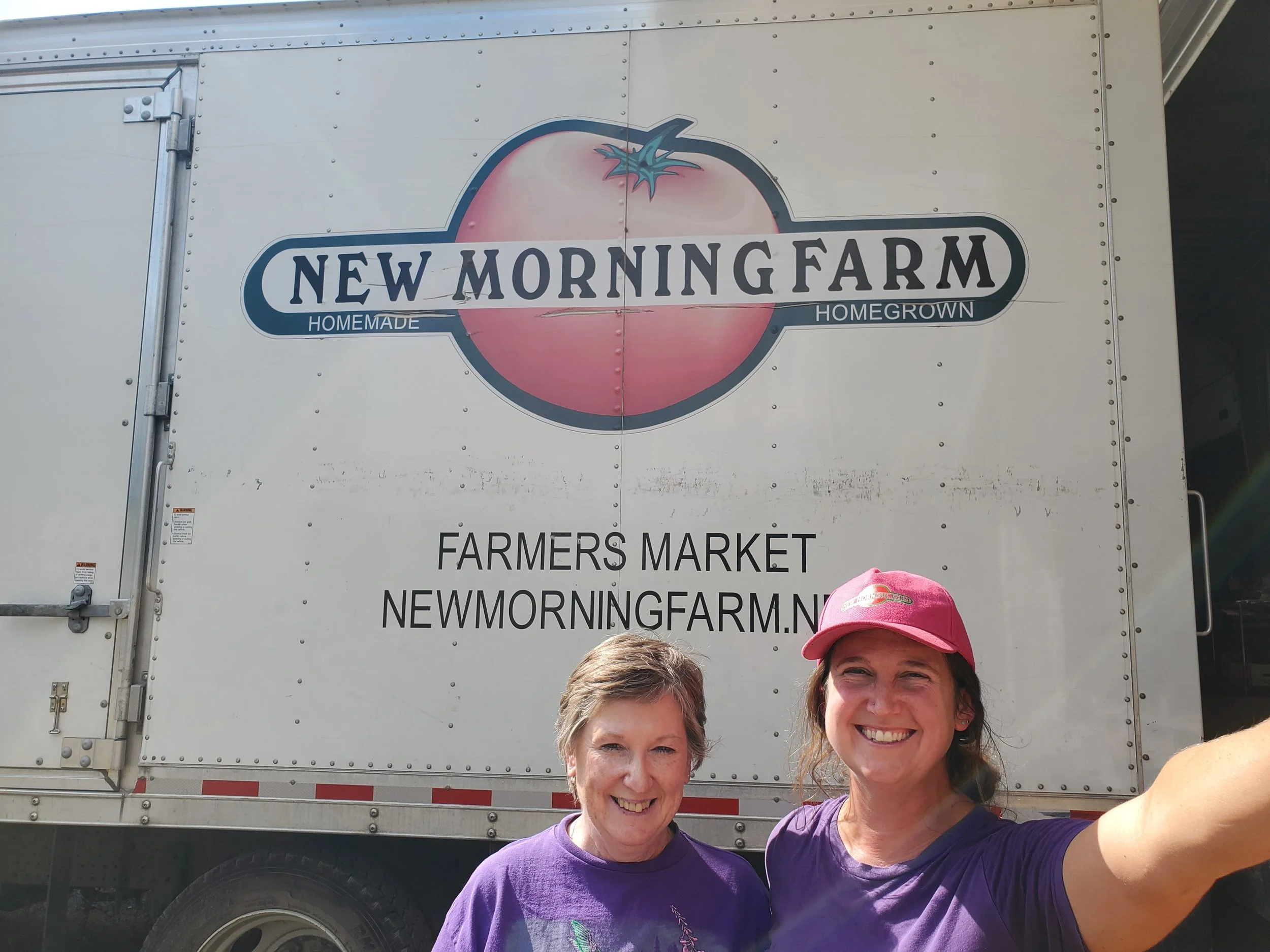 Catelan in pink New Morning Farm ballcap in front of market truck with Shirley