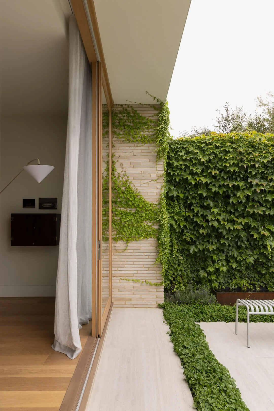 Architectural threshold at Silver House showing linen curtains, timber-framed glass doors, and climbing ivy on a modern brick facade.