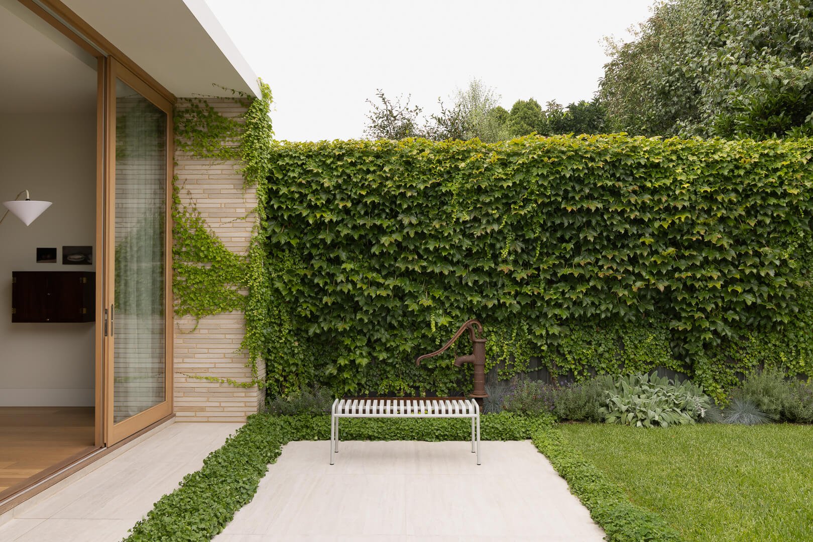 Restrained landscape design at Silver House featuring a repurposed heritage water pump as a garden water feature.