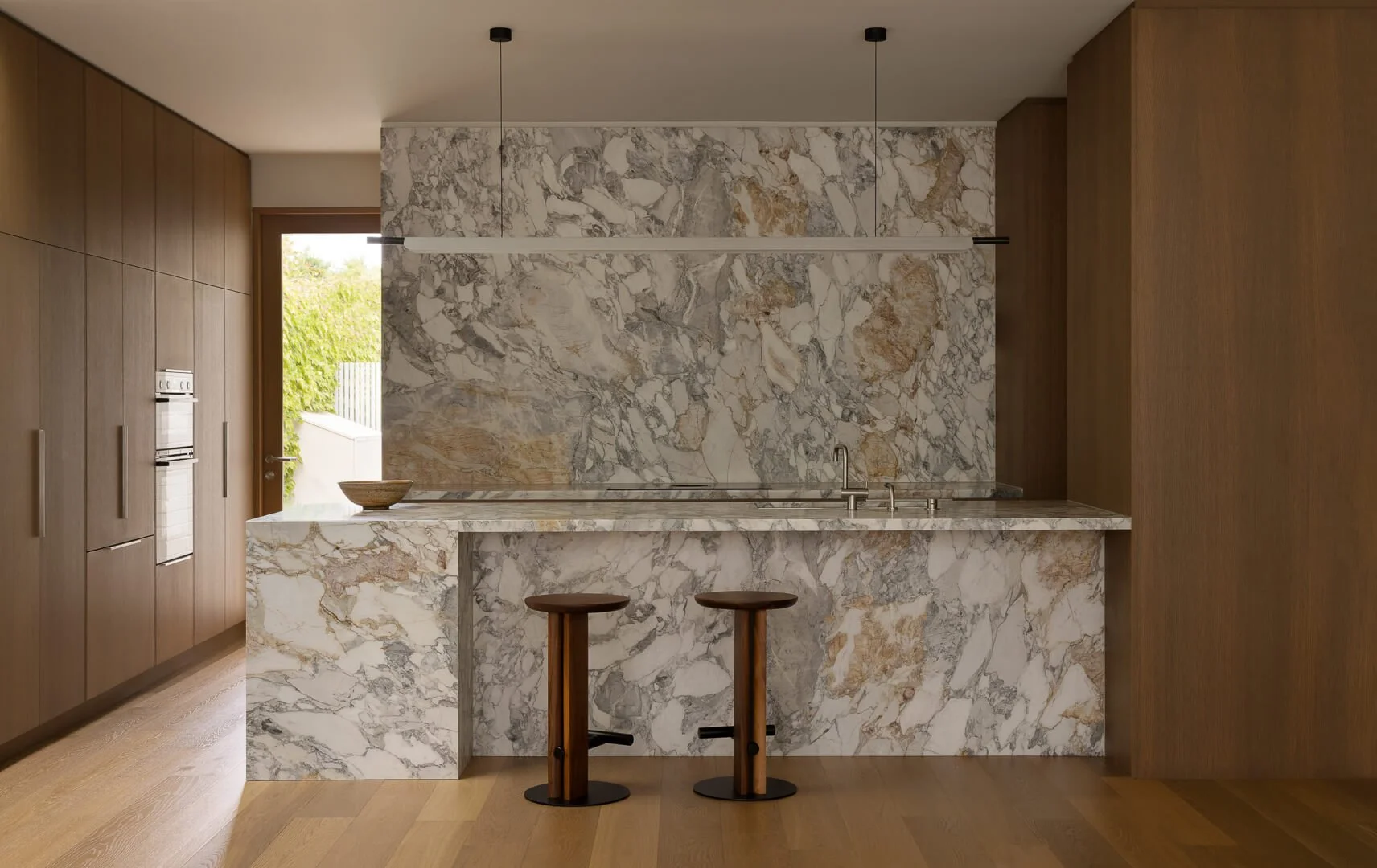 Full kitchen elevation at Silver House featuring a monolithic Kalana natural stone island and warm timber joinery by By Mysa.