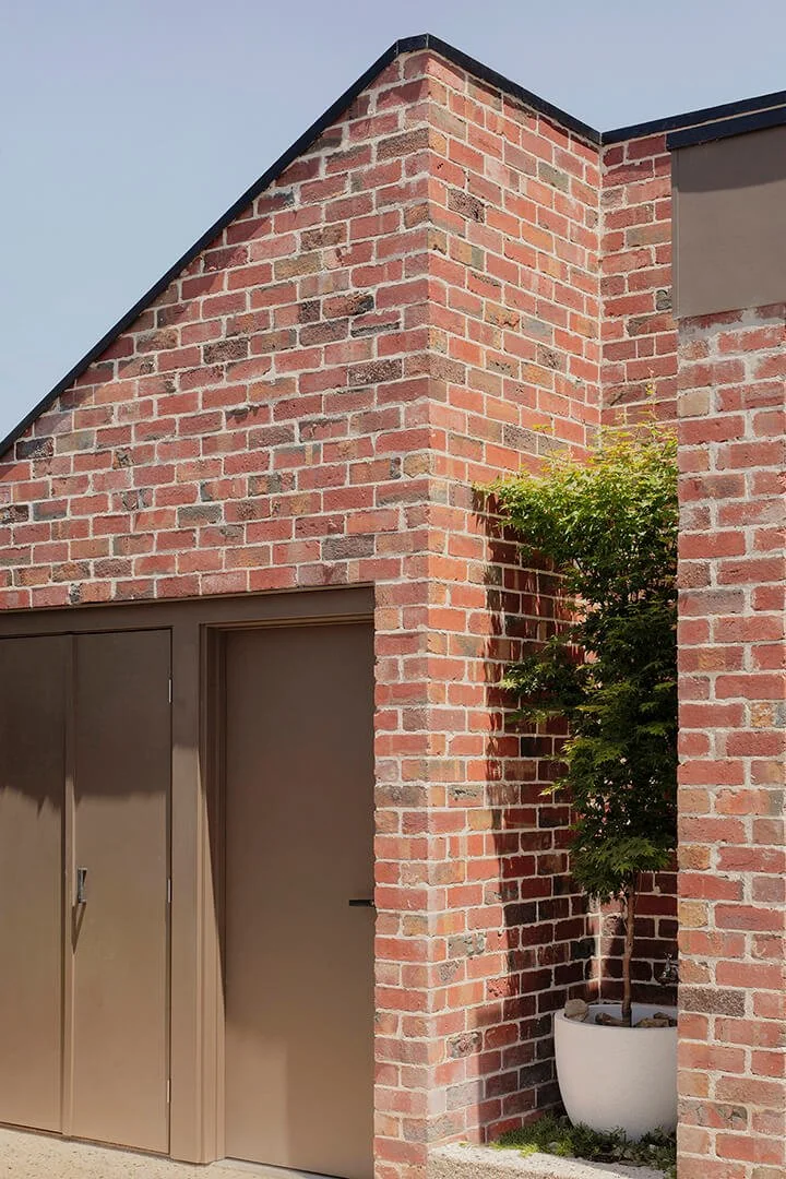 Red brick building with geometric architecture, featuring a brown door and a potted green tree, conveying a modern, clean aesthetic.