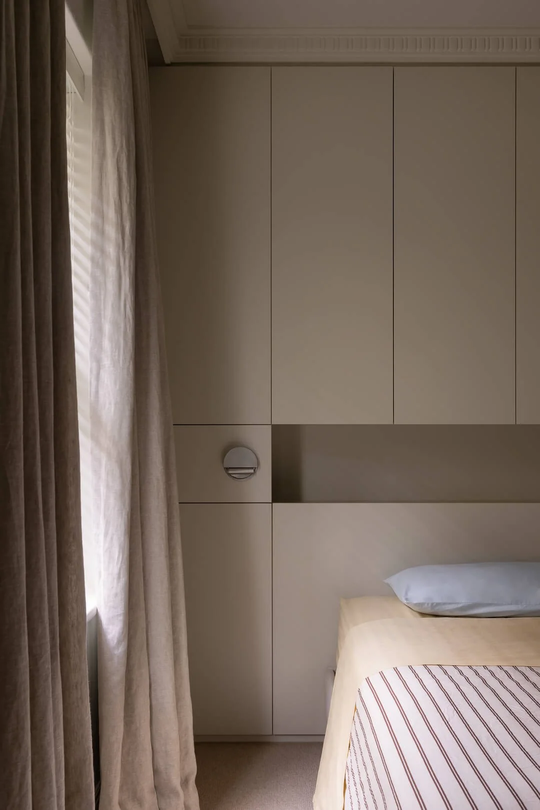 Detail of custom minimalist bedroom joinery with an integrated wall light and linen curtains at Silver House.
