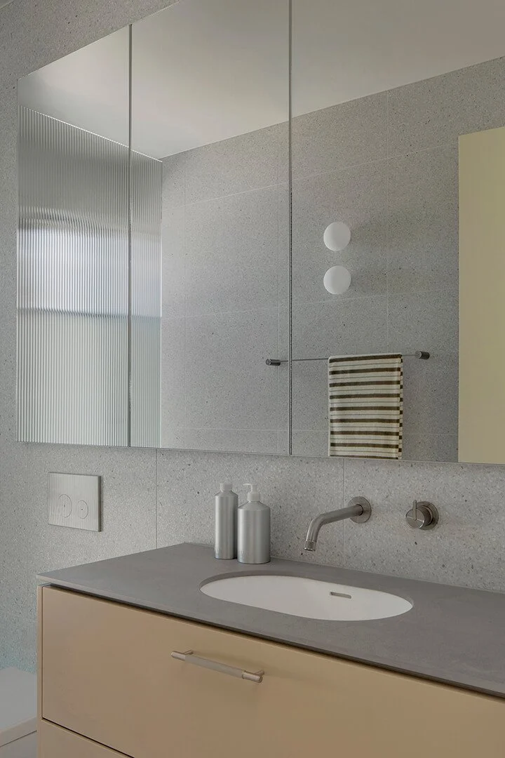 Modern bathroom with muted tones features a beige vanity, grey countertop, round sink, sleek tap, and mirrored cabinet. Minimal, calming ambiance.