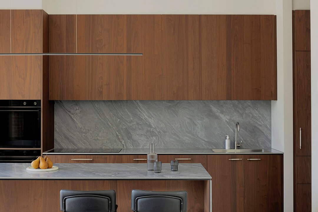Modern kitchen with dark wood timber veneer cabinets, a grey marble backsplash, and a countertop. A minimalist decor add a sleek, calm vibe.