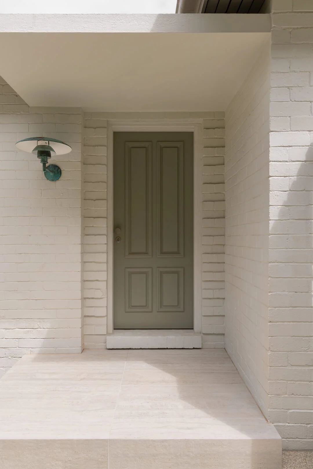Minimalist side entry at Silver House featuring a sage green door, white brickwork, and vintage-style outdoor lighting.