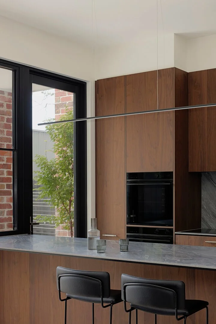 Modern kitchen with dark wood timber veneer cabinets, a grey marble backsplash, and a countertop. A minimalist decor add a sleek, calm vibe.