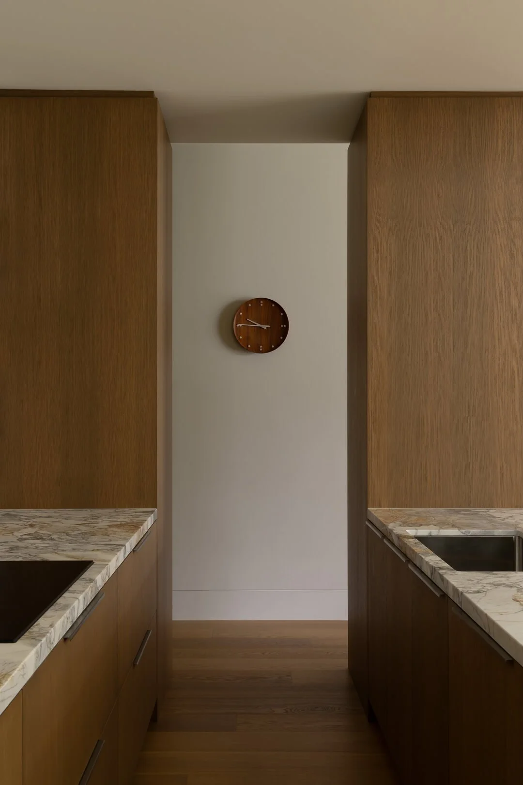Symmetrical kitchen sightline at Silver House featuring warm timber joinery, a mid-century wall clock, and Kalana natural stone benchtops.