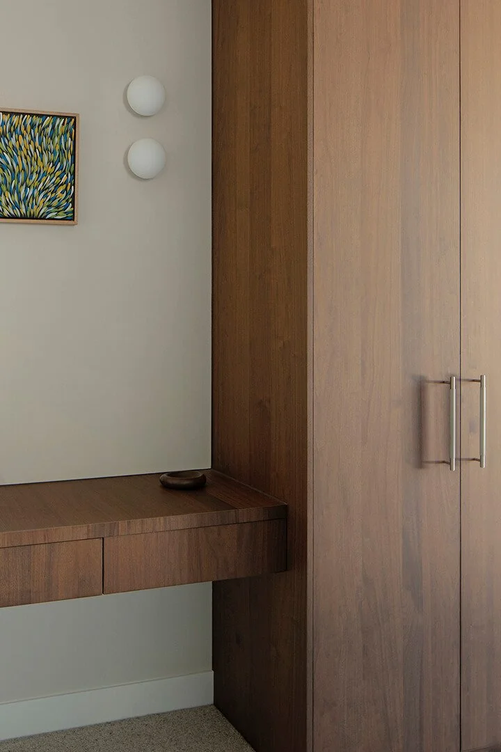 Minimalist interior with a wooden desk and cabinet, featuring abstract wall art and two round white lights. Neutral tones create a serene ambiance.