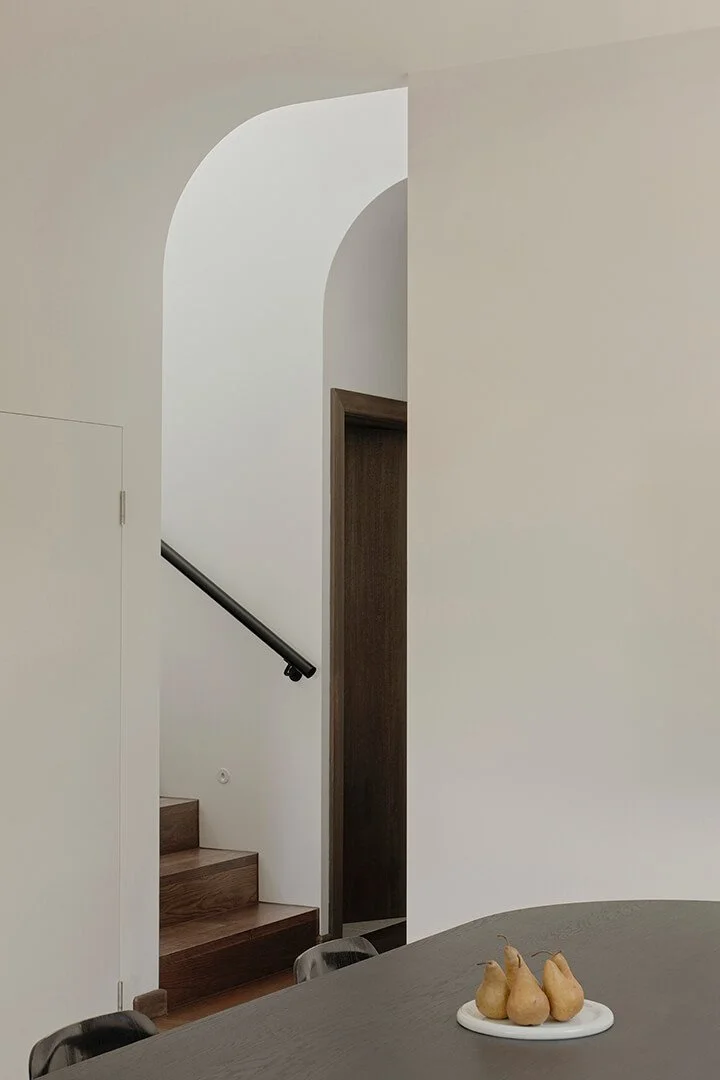 Minimalist interior with a curved archway and wooden staircase, and light well above, creating a serene and modern atmosphere.