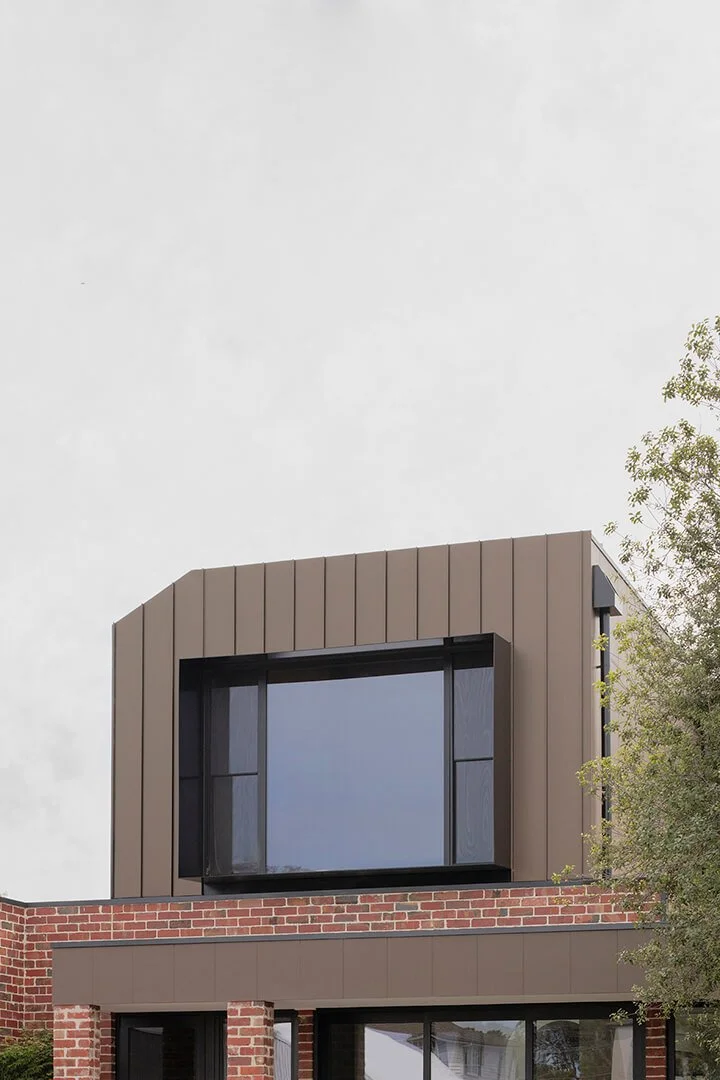 Modern building exterior with geometric design. Bronze metal cladding and large rectangular window, sitting on a recycled brick base. Moody Architectural Photography