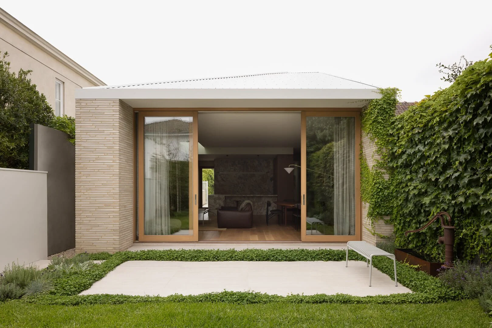 Rear elevation of Silver House featuring large timber sliding doors and a white corrugated iron roof extension by By Mysa.